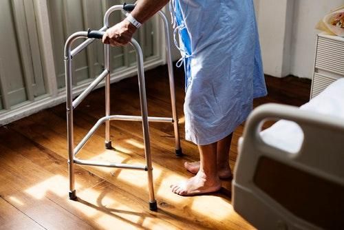 person in hospital gown holding onto walker