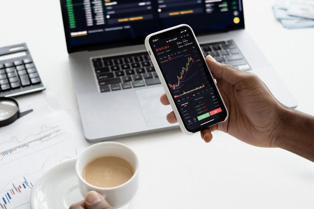 person looking at stock charts on their phone while drinking coffee