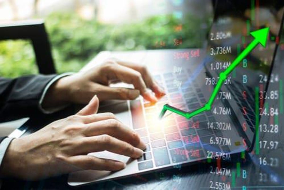 Person's hands using laptop with stock tickers in the foreground.
