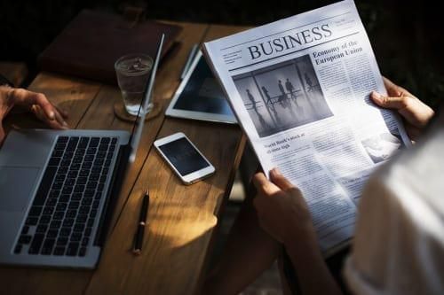 person sitting at a desk reading business section of newspaper