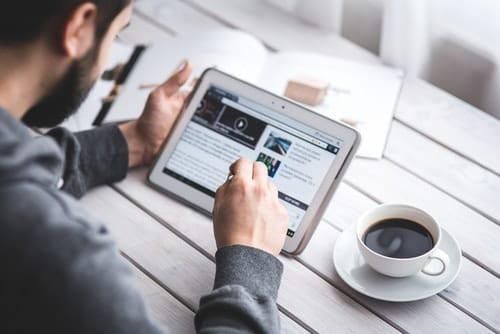 person using tablet to read news while they have a coffee