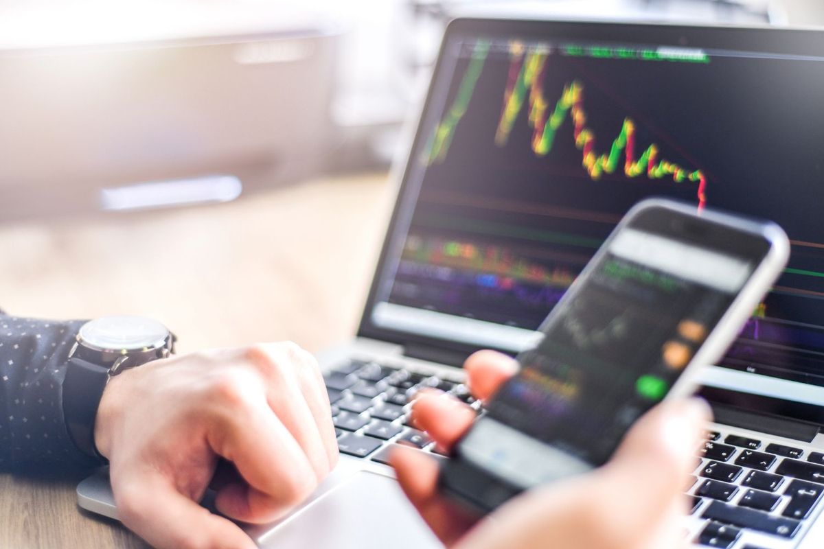 Person viewing stock charts on a laptop and smartphone.