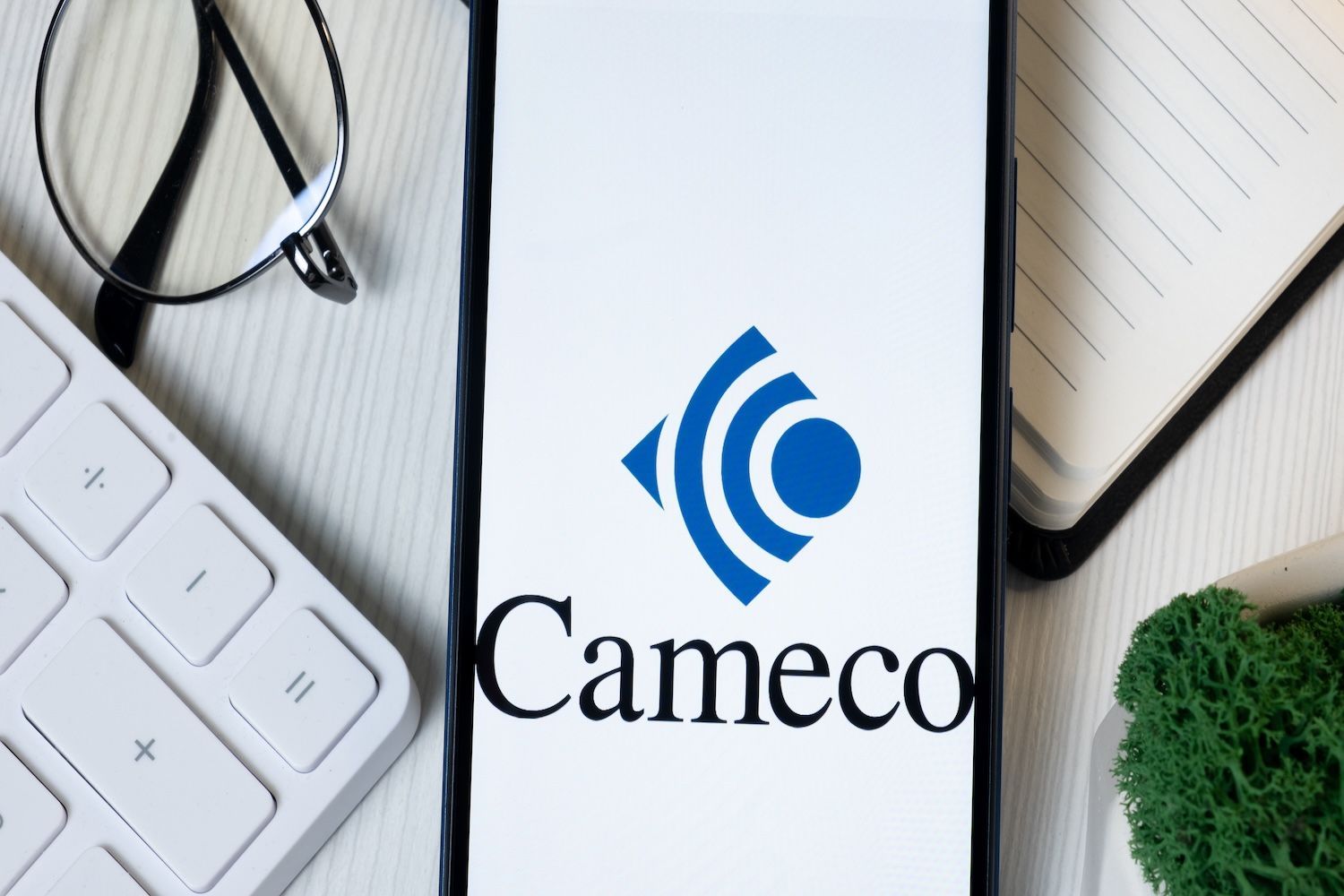 Phone displaying Cameco logo beside glasses and keyboard.