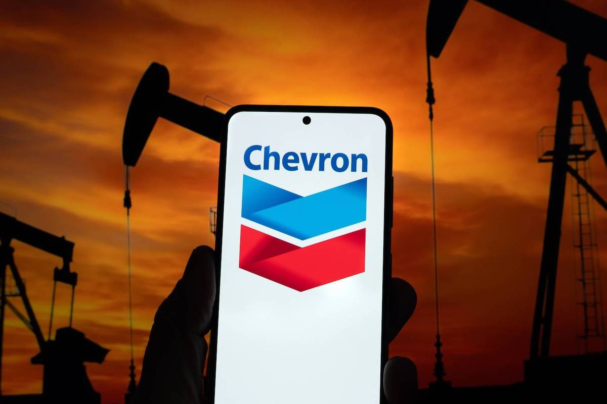 Phone displaying Chevron logo against oil pumps and sunset background.