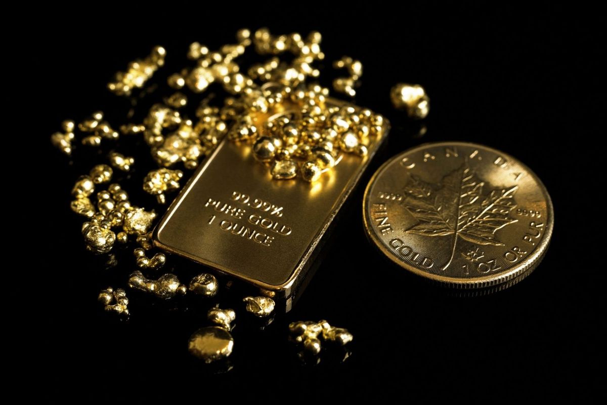 Physical gold bar and gold Maple Leaf coin with small gold nuggets on top.