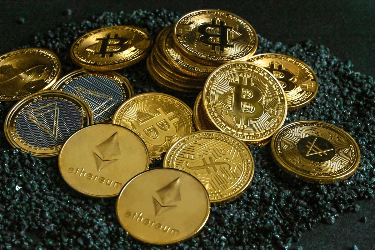 Pile of gold cryptocurrency coins, including Bitcoin and Ethereum, on a dark textured surface.