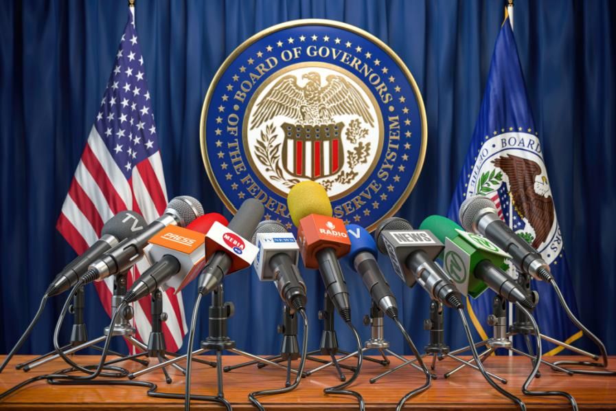 Press microphones in front of Federal Reserve seal and U.S. flag.