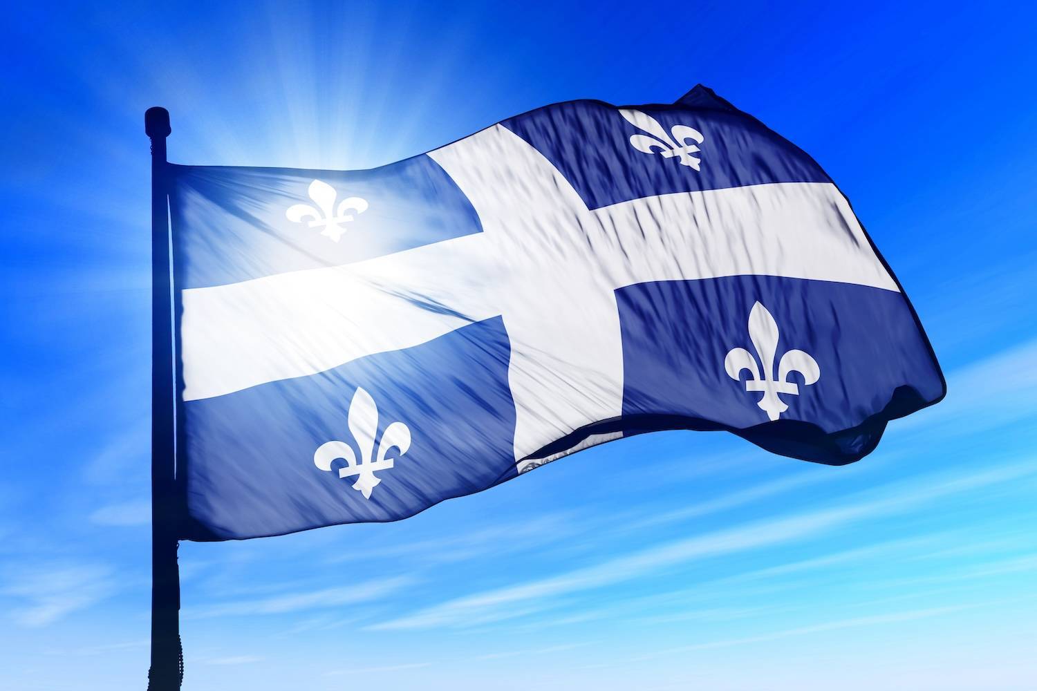 Québec flag waves against bright blue sky.