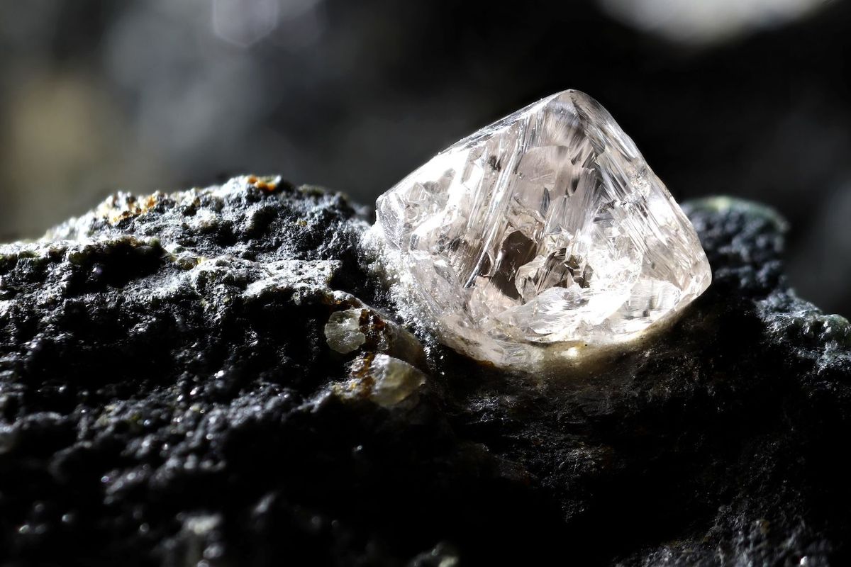Raw diamond resting on a textured dark rock surface.