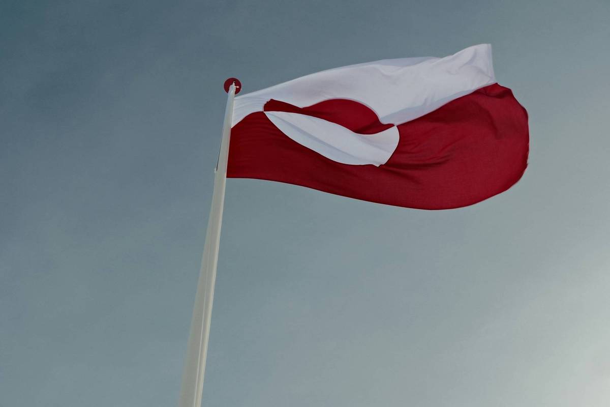 Red and white flag waving on a tall pole against a clear, grayish sky.