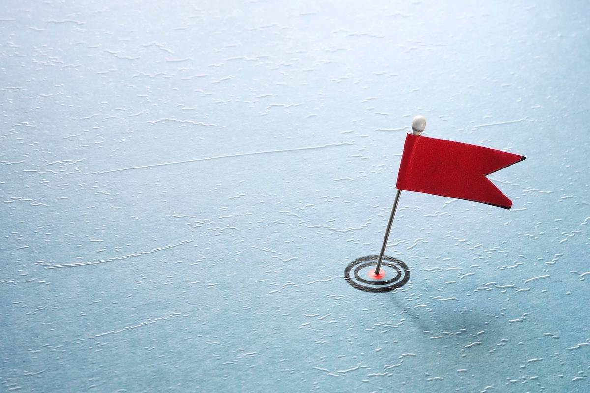 Red flag pin stands on textured blue surface with target-like circle at its base.