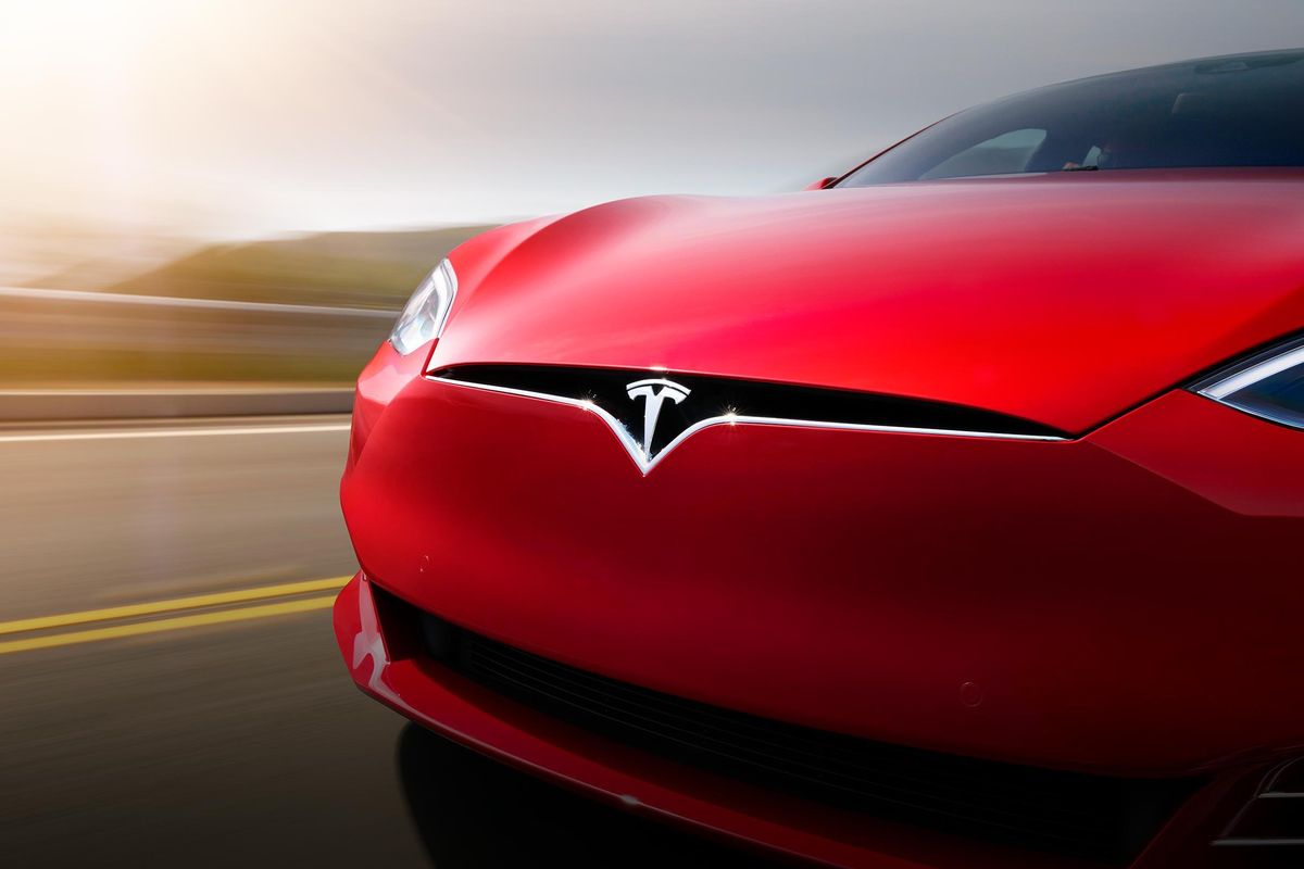 Red Tesla car driving on the road close up.