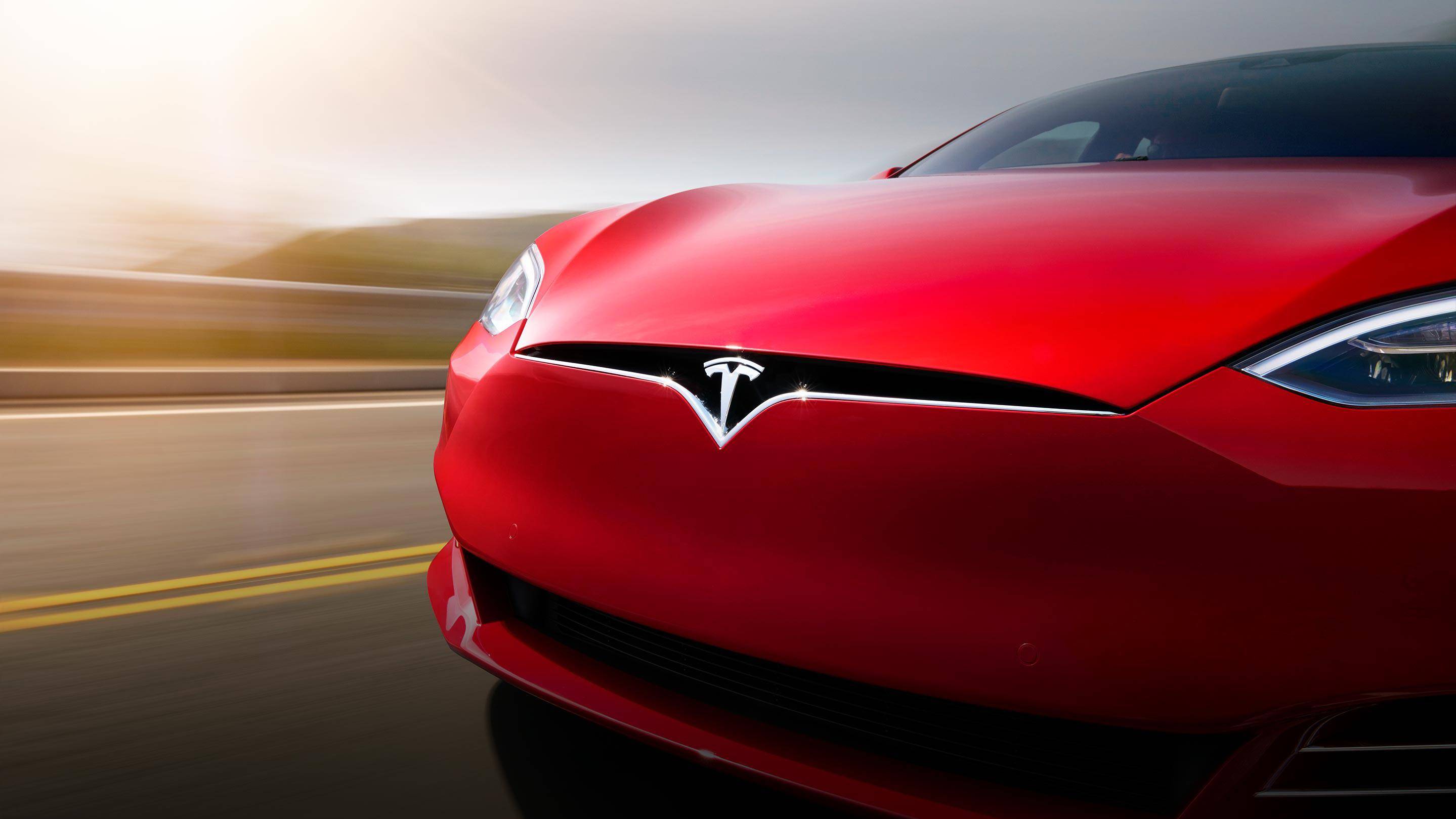 Red Tesla car driving on the road close up.