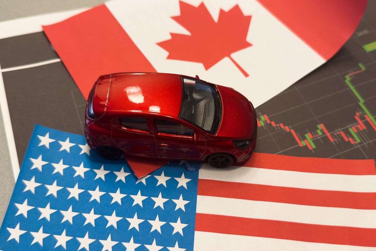 Red toy car on US and Canadian flags, financial chart in background.