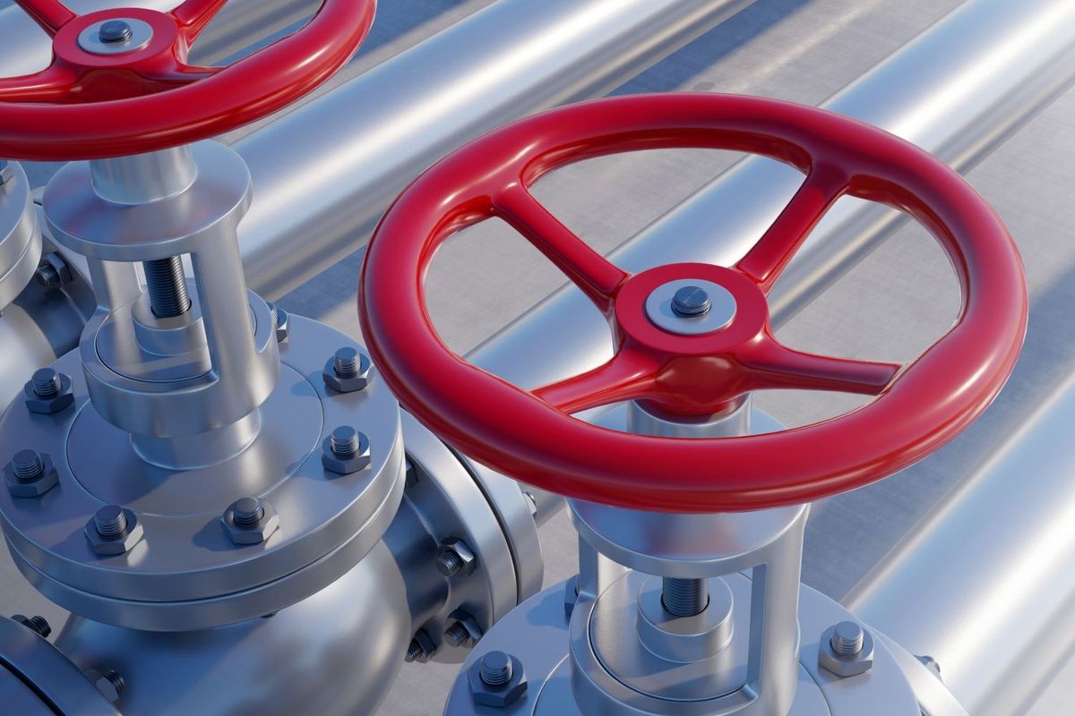 Red valve handles on industrial metal pipes.