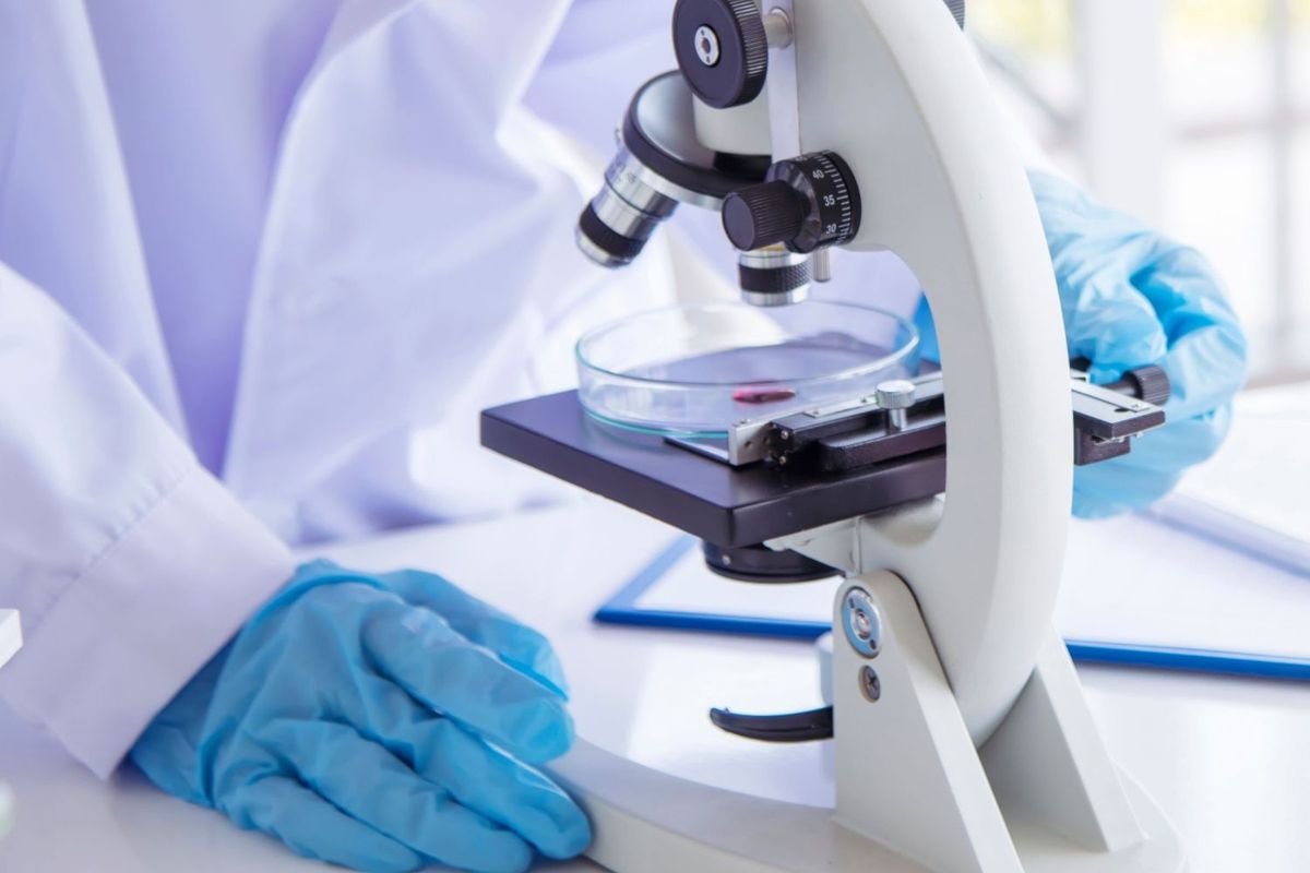 Researcher in medical lab looking at sample with microscope.