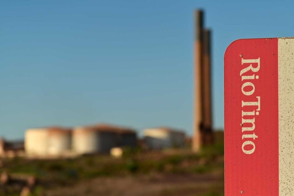 Rio Tinto sign with industrial backdrop and tanks under a clear blue sky.