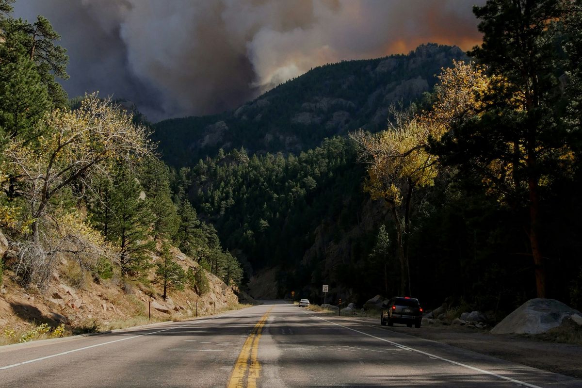 Road through forest with heavy smoke from distant wildfire in the mountains.