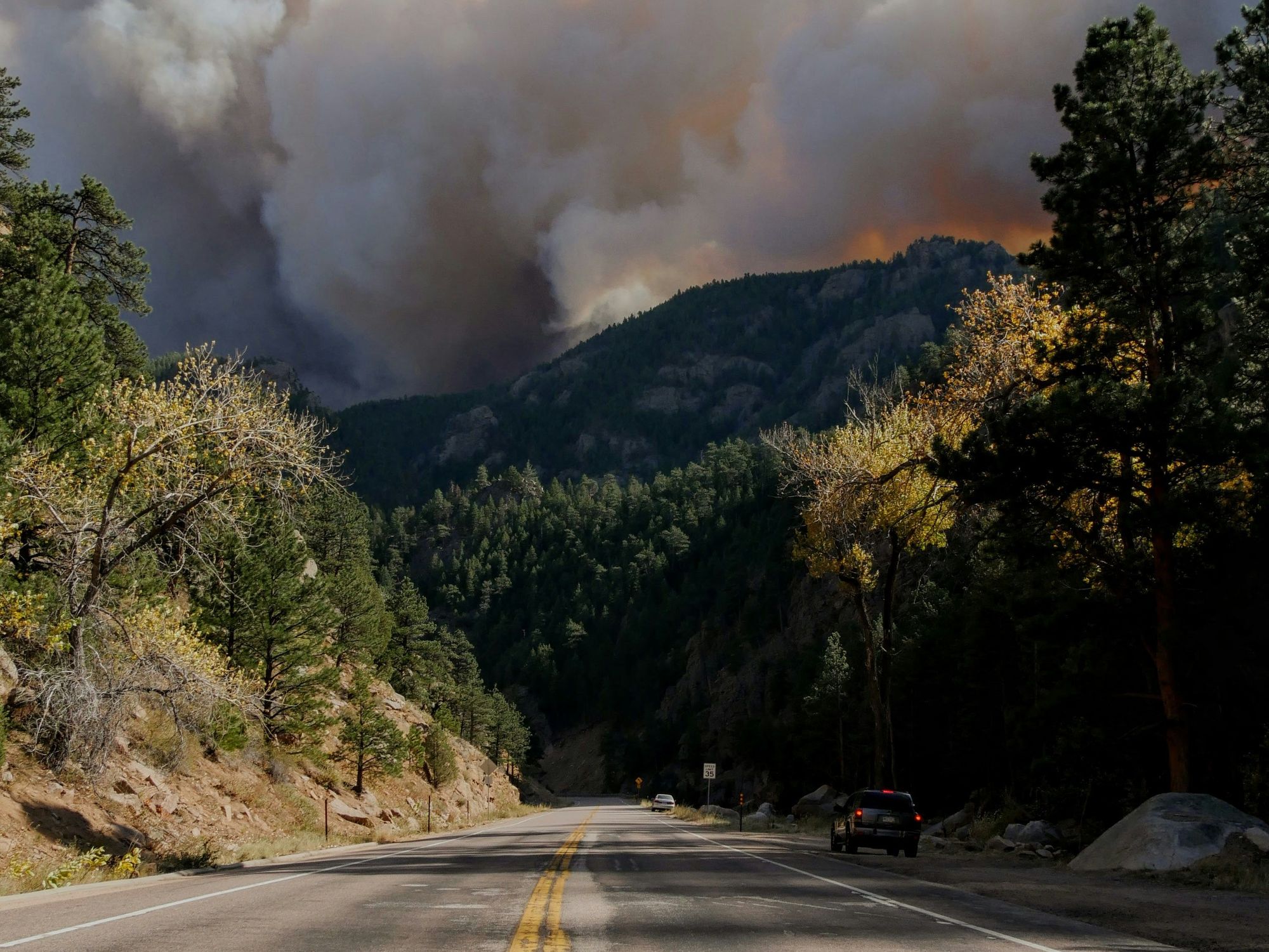 Road through forest with heavy smoke from distant wildfire in the mountains.