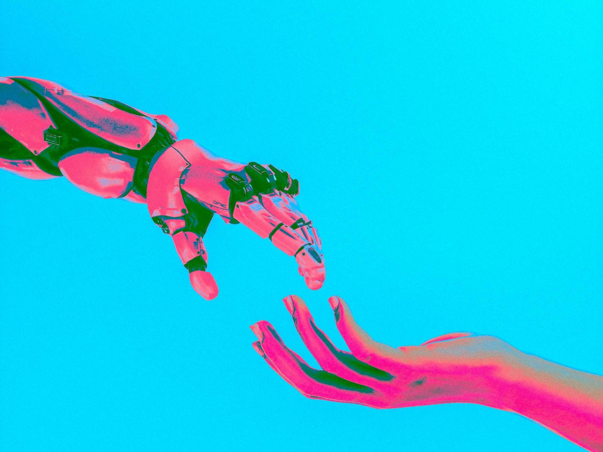 Robotic hand reaches toward human hand against a bright cyan background, both tinted in pink hues.