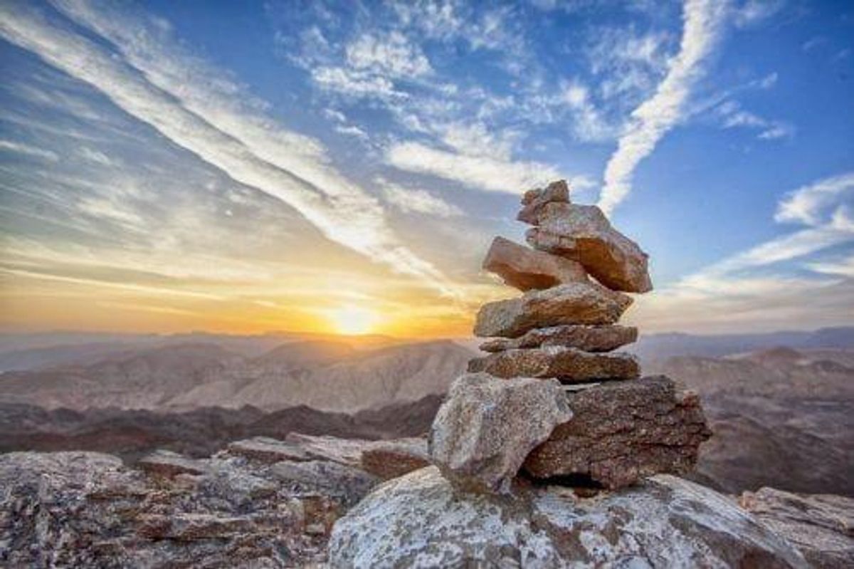 rocks stacked high in the foreground while the sun rises over mountains