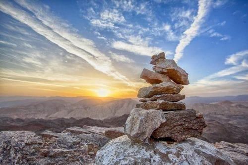 rocks stacked high in the foreground while the sun rises over mountains