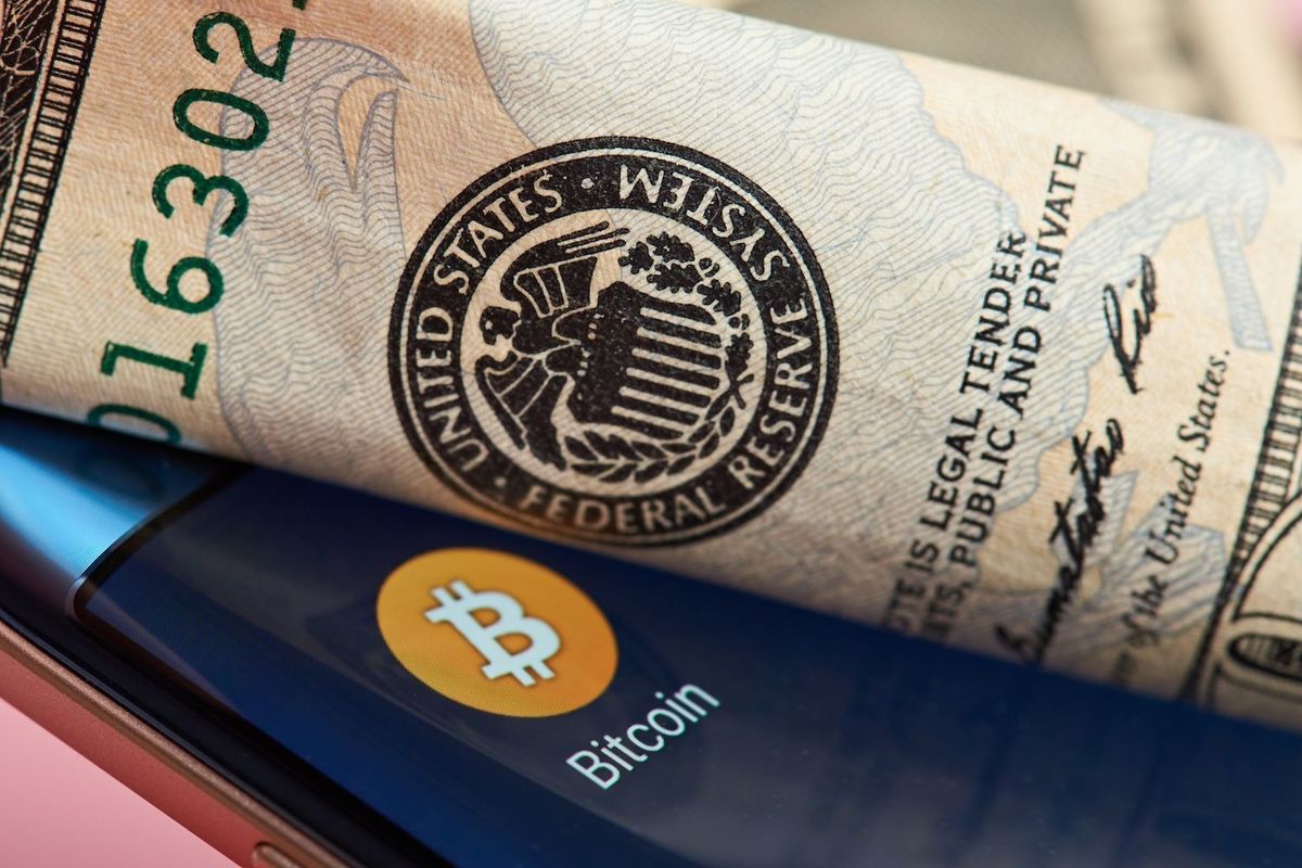 Rolled dollar bill on phone screen displaying the Bitcoin logo.