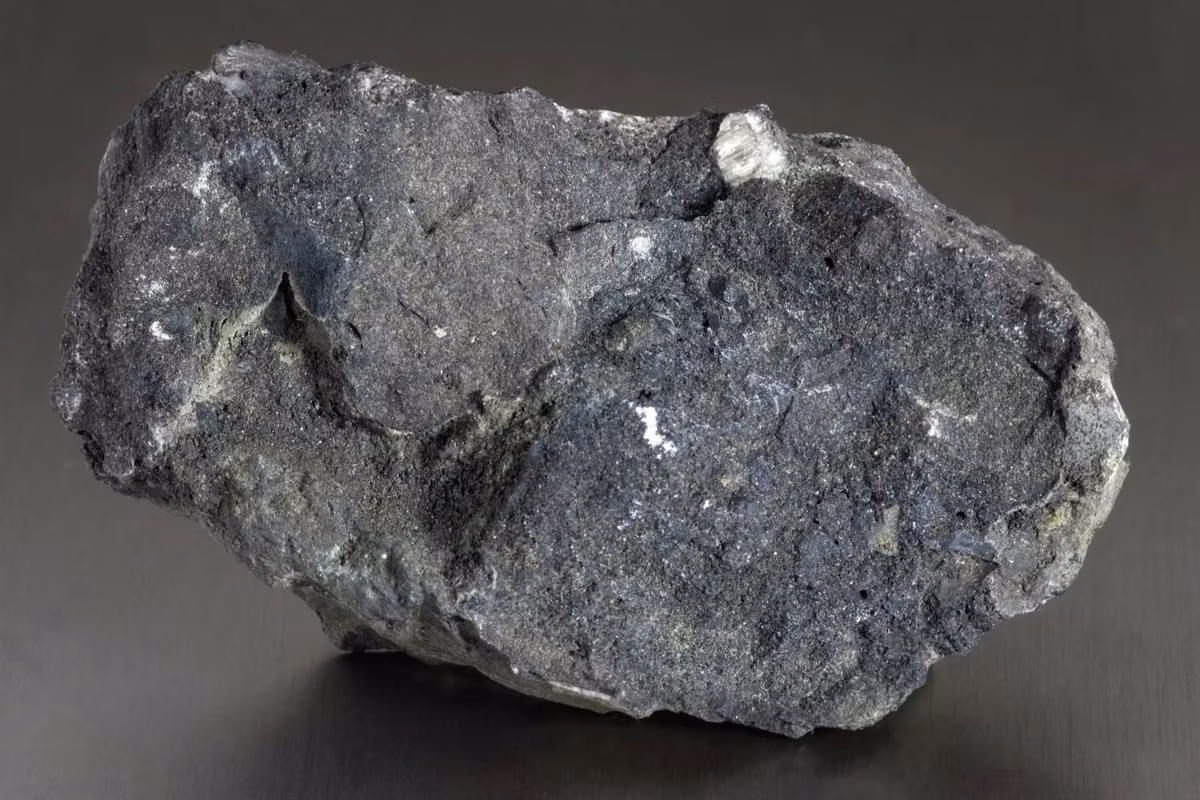 Rough, dark gray sedimentary phosphate rock with jagged texture sits on a smooth, dark gray surface.