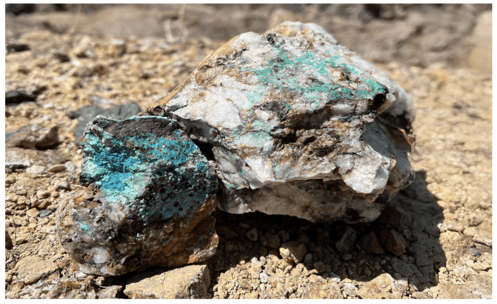 Rough turquoise stone with a mix of blue and earthy tones on rocky ground from Oreterra Metals' Kinkaid project