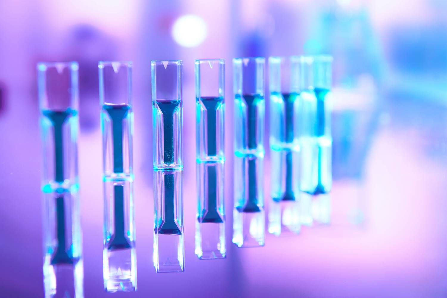 Row of blue-lit test tubes with a blurred purple background.