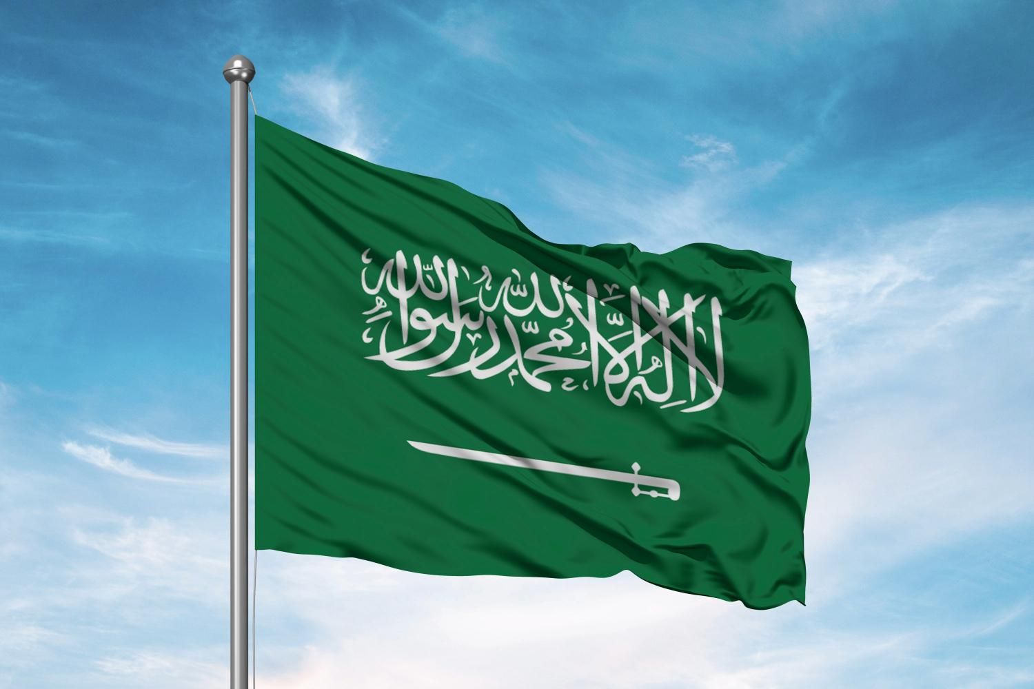 Saudi Arabian flag waving against a blue sky.