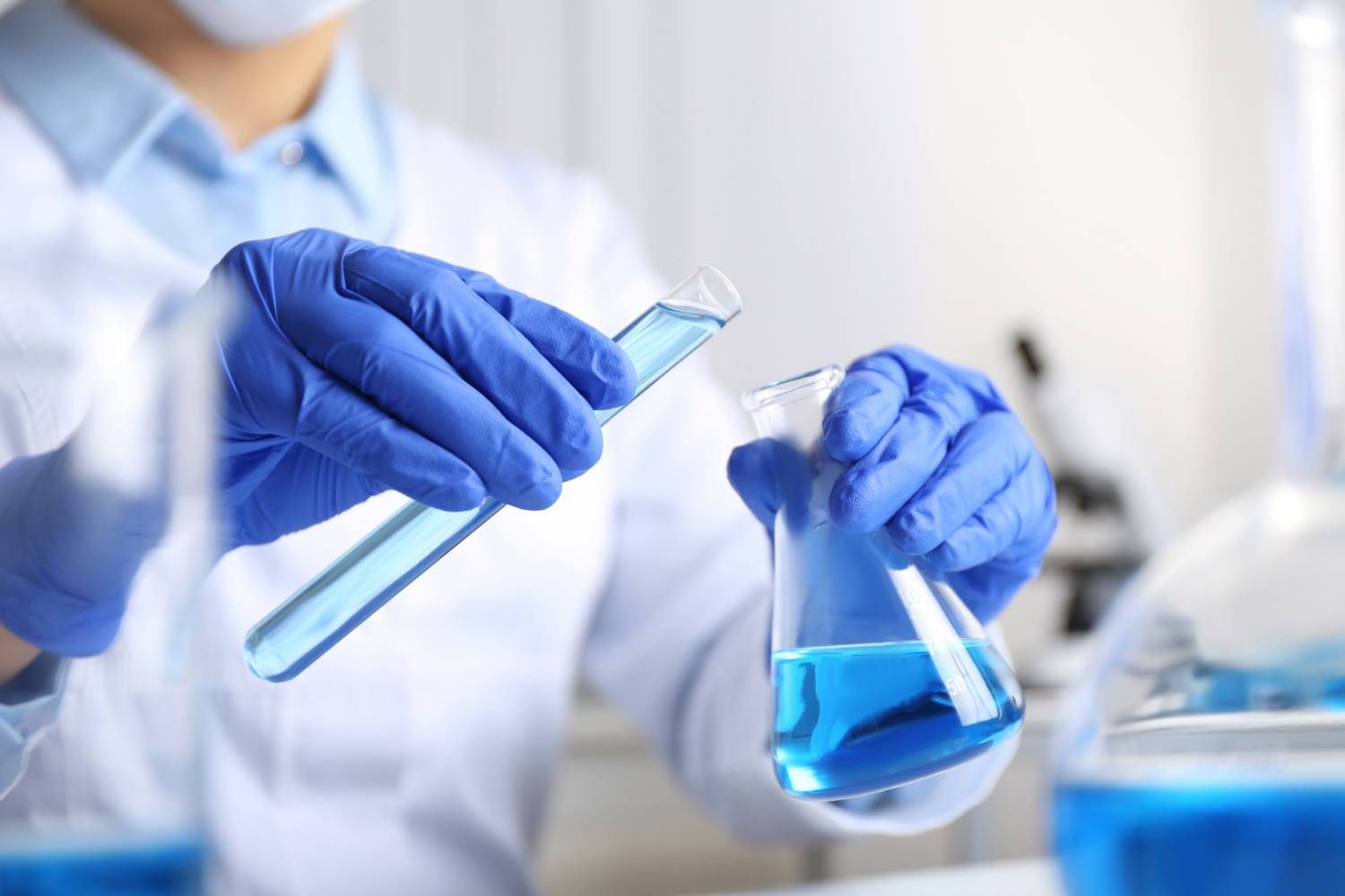 Scientist pouring blue liquid from a test tube into a flask in a lab.