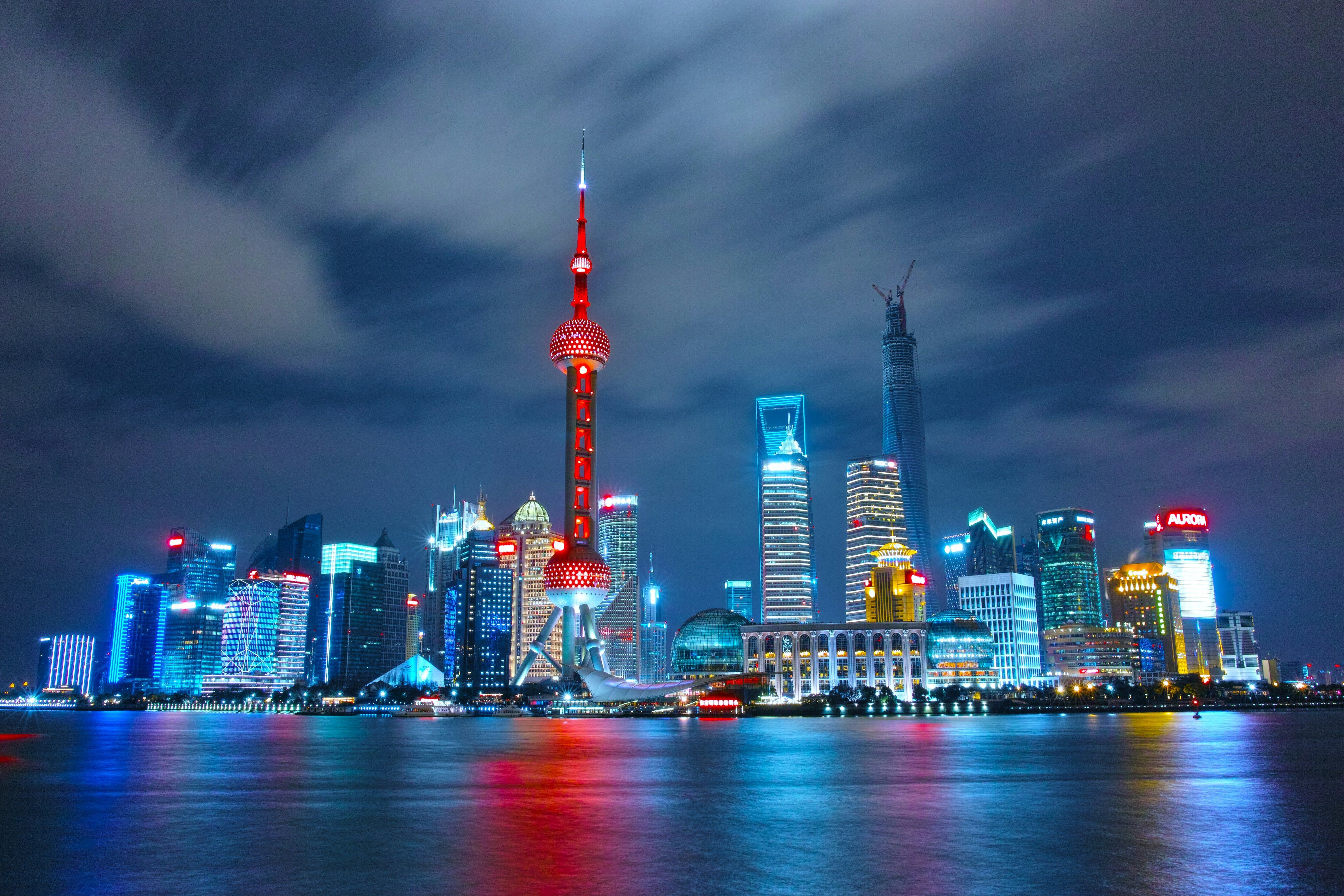 Shanghai skyline at night, vibrant lights reflecting on the Huangpu River.