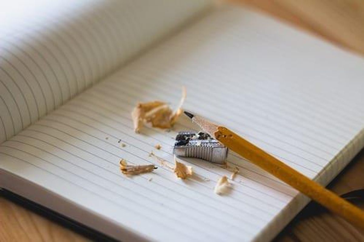 sharpened pencil, silver pencil sharpener and shavings on an opened lined paper notebook