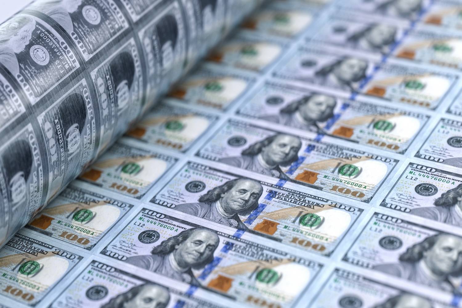 Sheets of printed US$100 bills over a cylinder on a printing press.