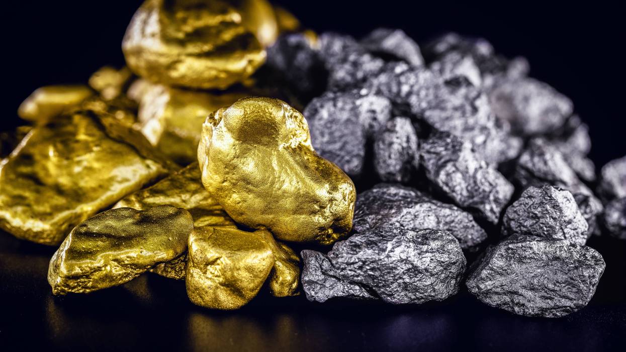 Shiny gold nuggets piled next to silver nuggets on a black surface.