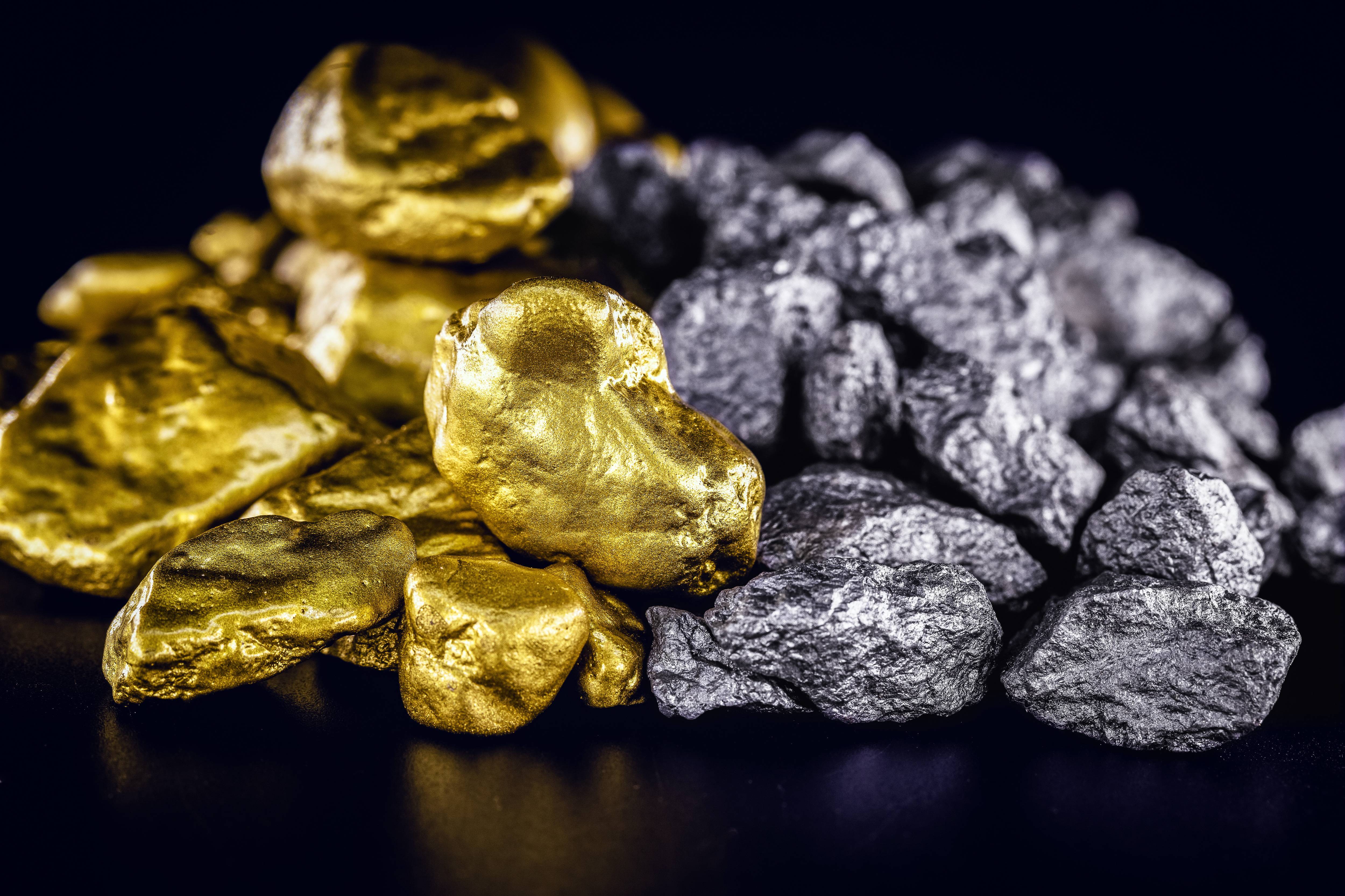Shiny gold nuggets piled next to silver nuggets on a black surface.