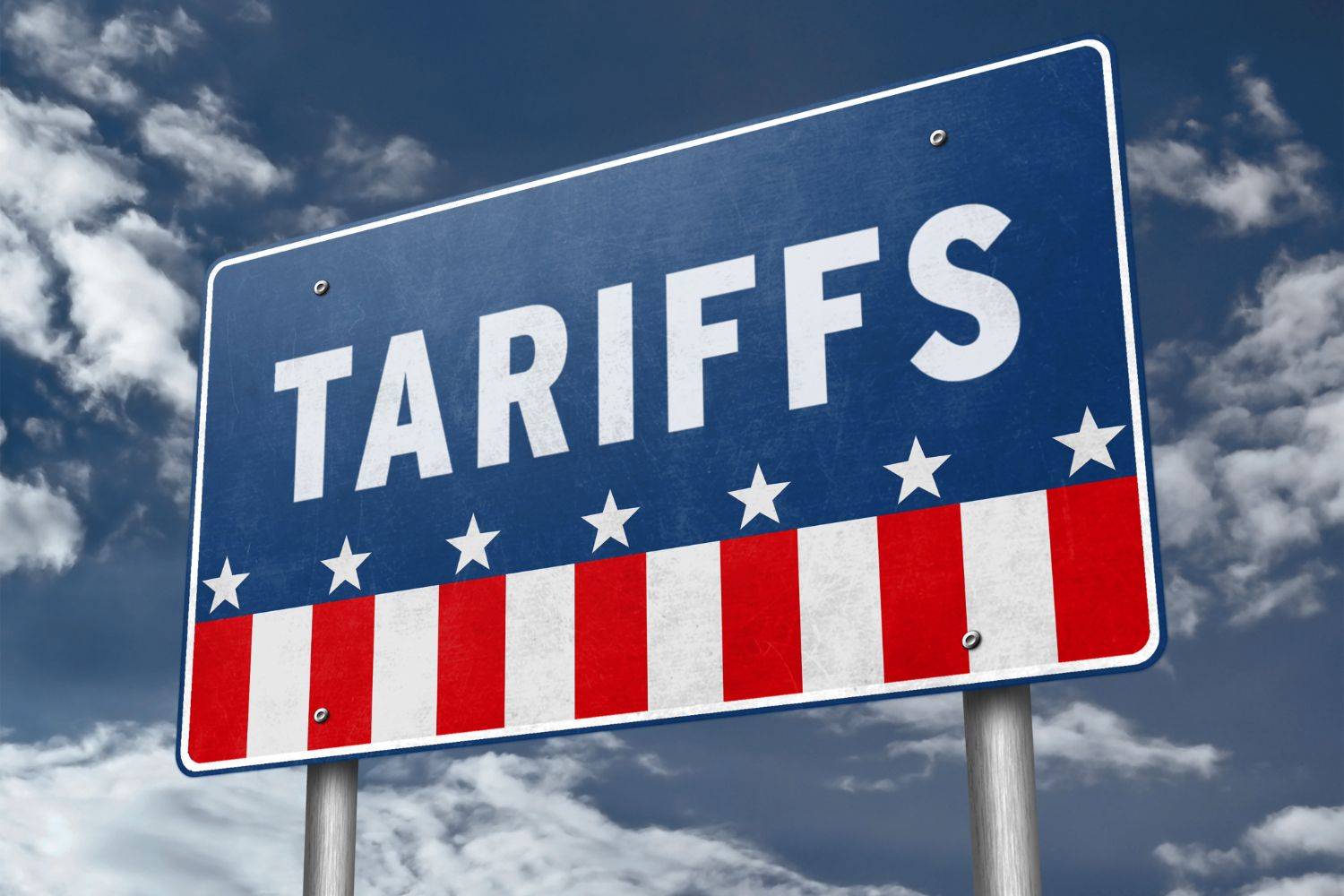 Sign reading "Tariffs" with stars and stripes design under a cloudy sky.
