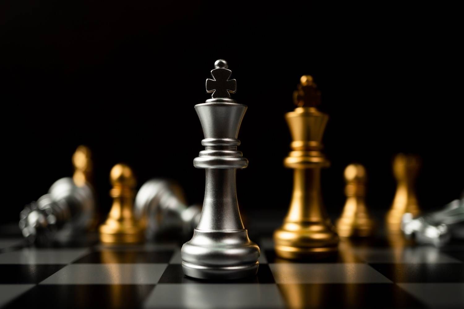 Silver and gold chess pieces on a board with a dark background.