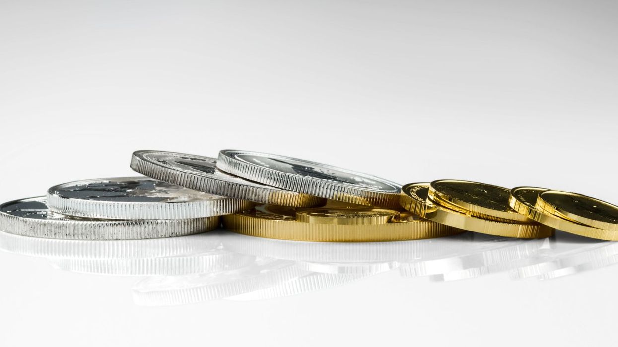 Silver and gold coins stacked on a reflective surface.