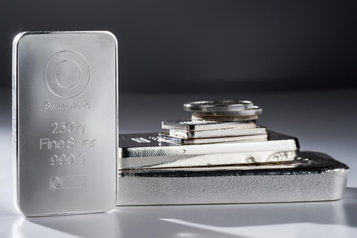 Silver bar and stacked coins on reflective surface.