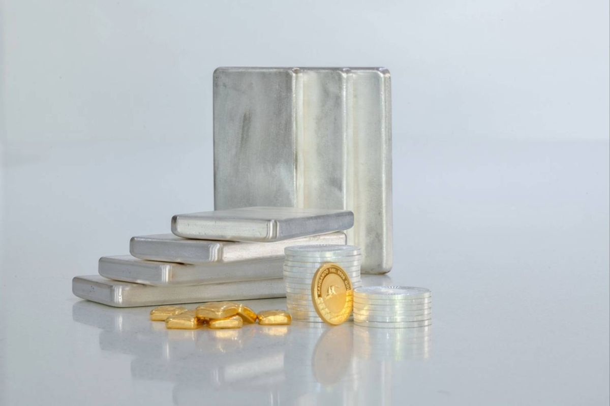 Silver bars and coins stacked with gold coins on a reflective surface.