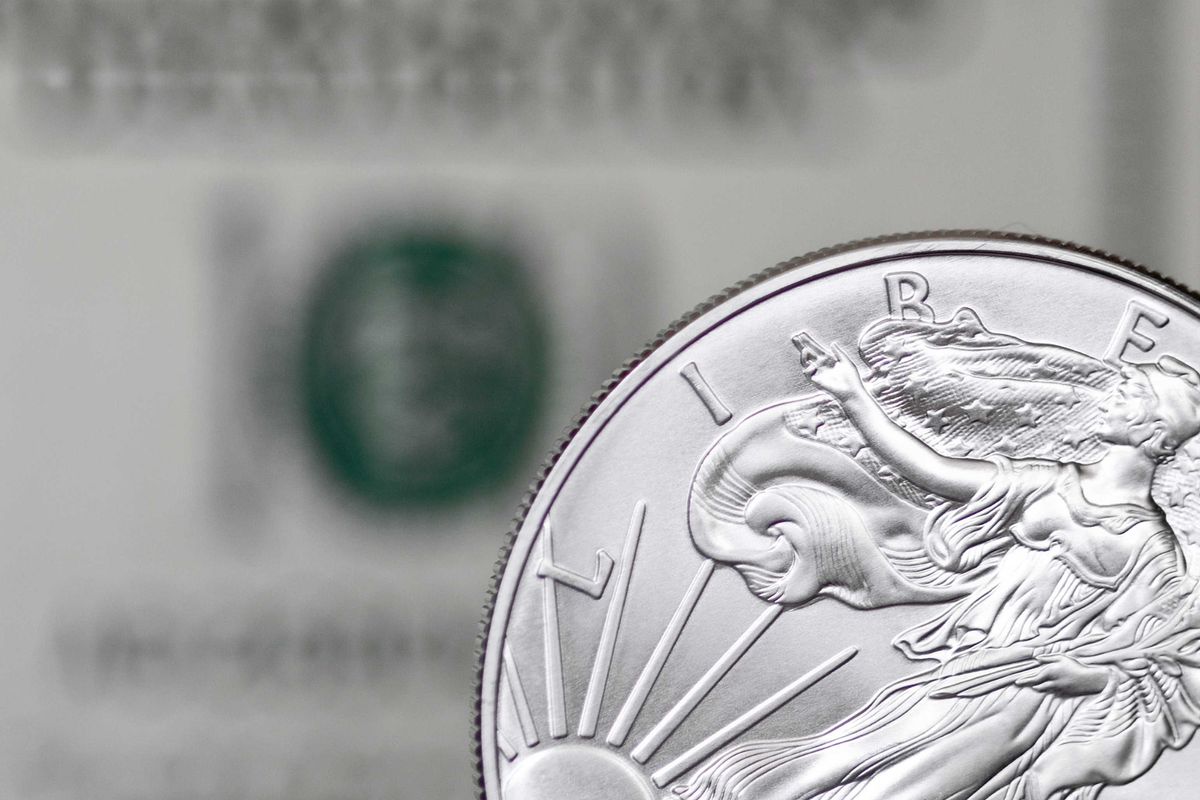 Silver coin with Liberty design in front of blurry dollar bill background.