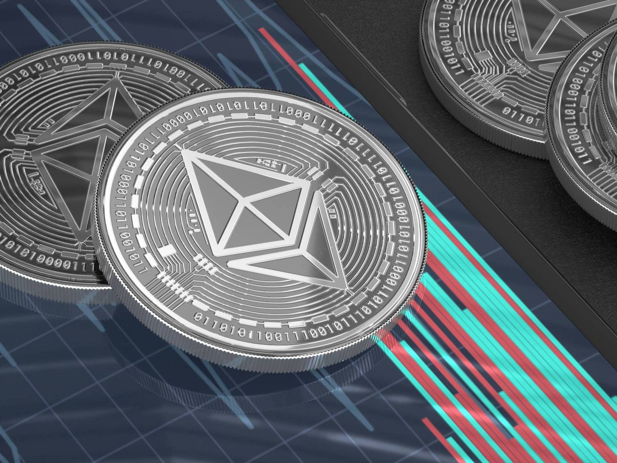 Silver cryptocurrency coins with geometric designs rest on a tablet displaying a digital chart with green and red lines.