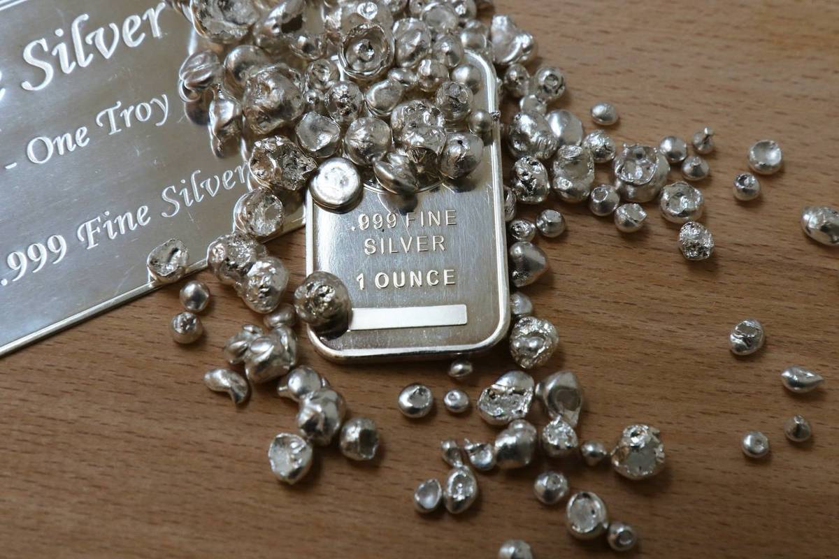 Silver nuggets scatter over a wooden surface with a silver bar reading: 999 Fine Silver, 1 Ounce.