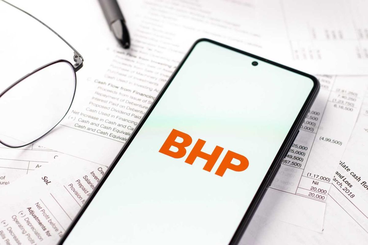 Smartphone displaying "BHP" logo on documents, near glasses and pen.