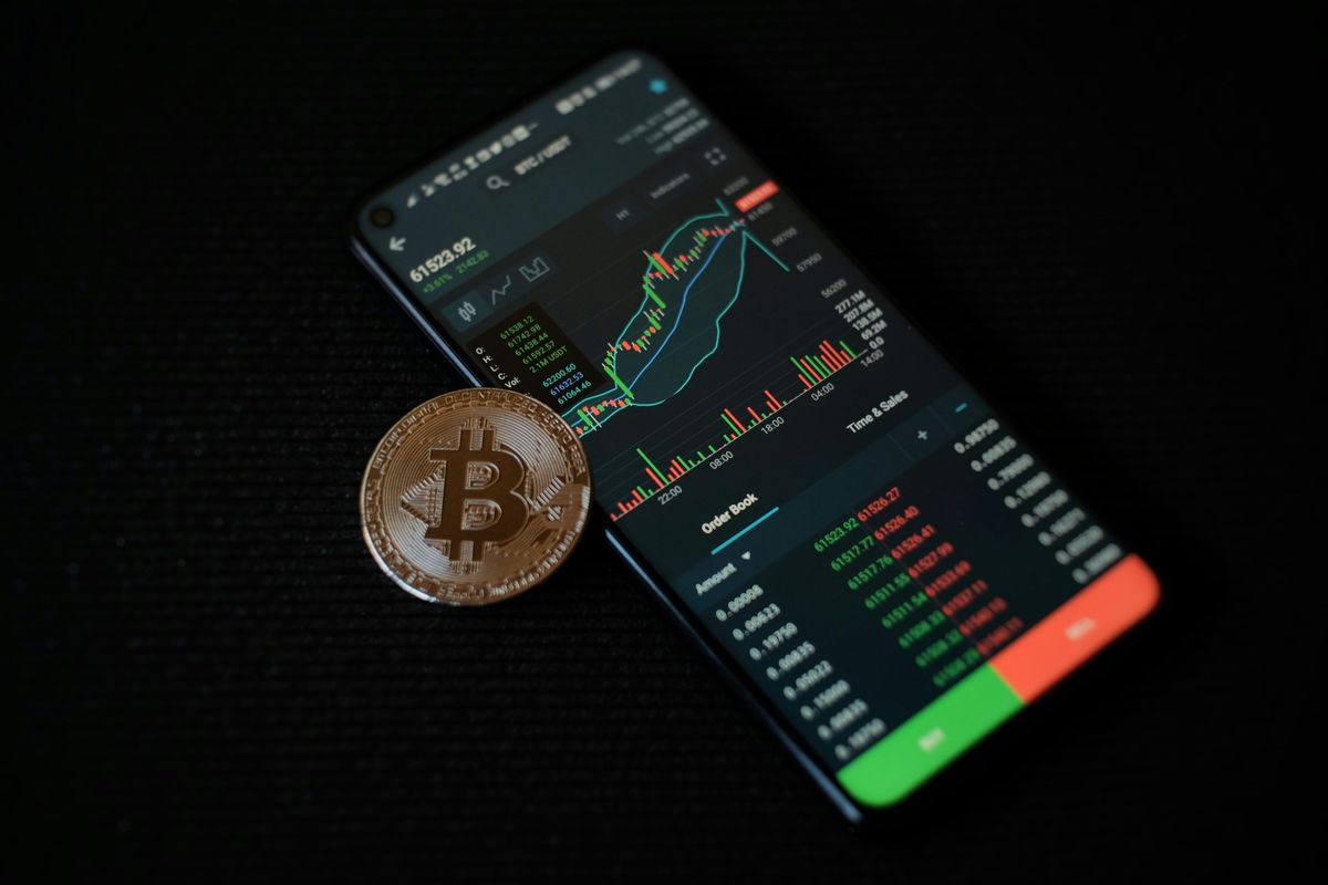 Smartphone displaying crypto charts with a Bitcoin coin on a black background.