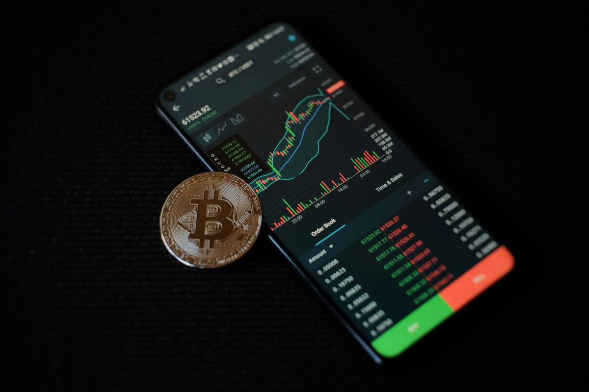 Smartphone displaying crypto charts with a Bitcoin coin on a black background.