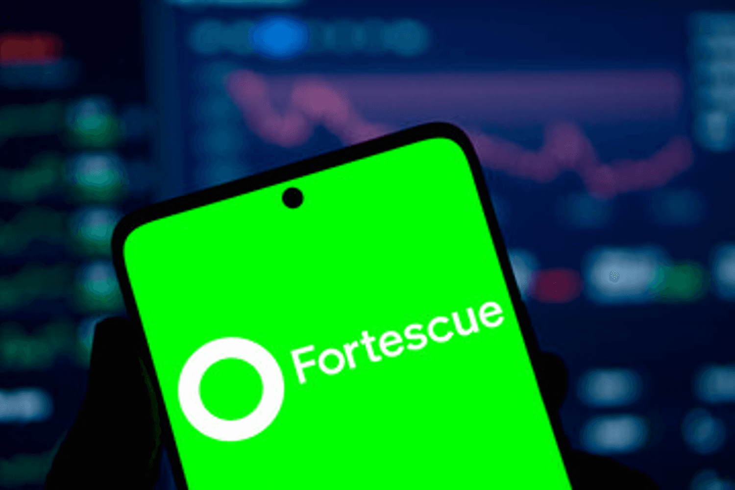 Smartphone displaying "Fortescue" on a green screen, with stock charts in the background.