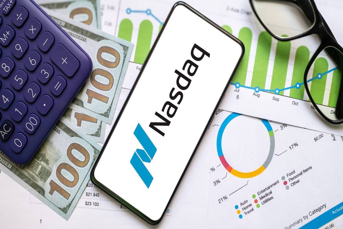 Smartphone displaying "Nasdaq" sits on charts beside a purple calculator, glasses and dollar bills.